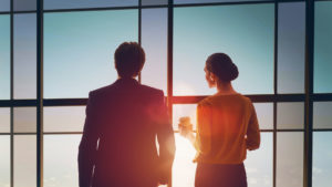 Professional Couple standing at office window at sunrise